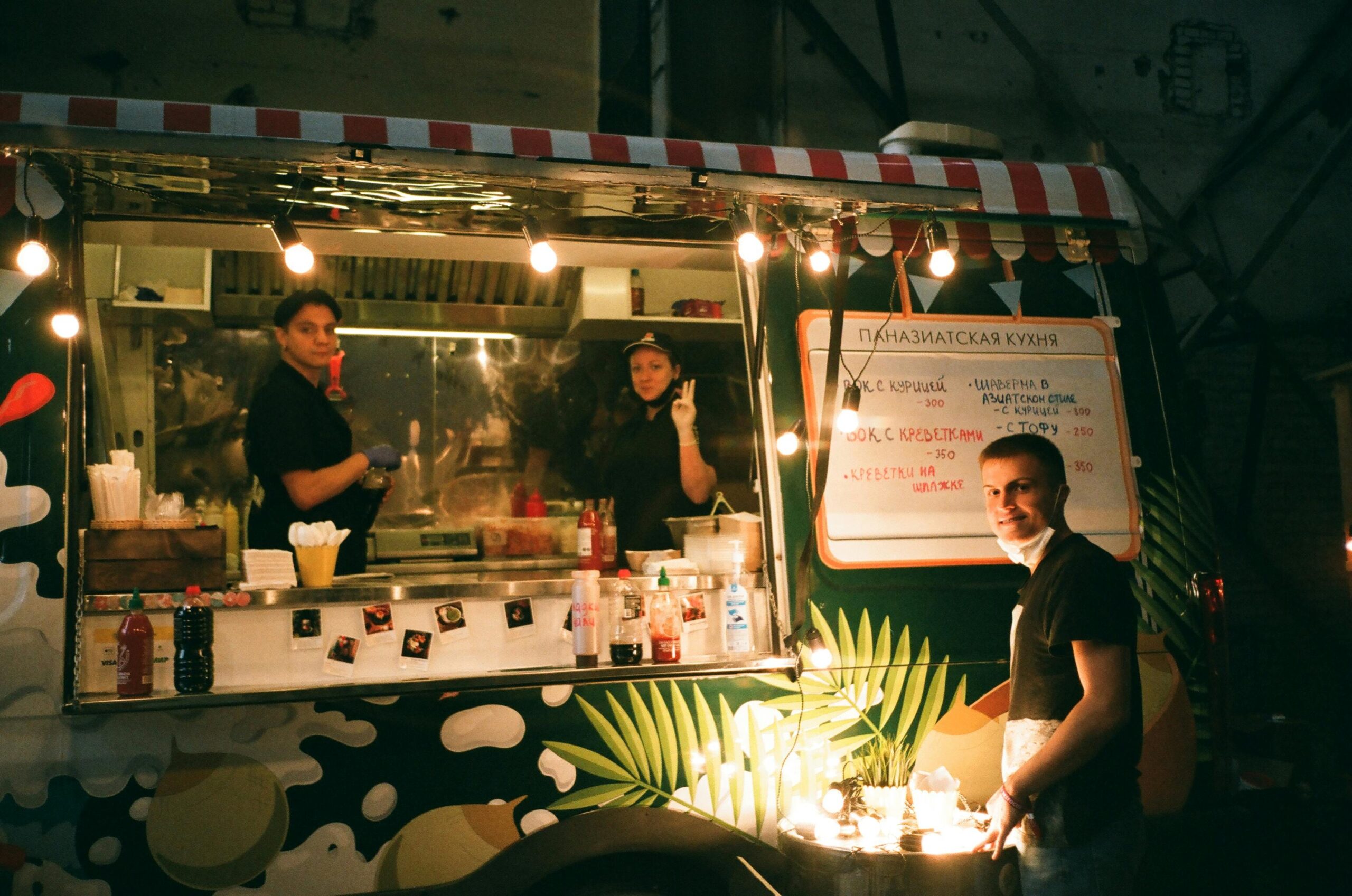 Group of coworkers standing near street food truck while working and looking at camera at nights